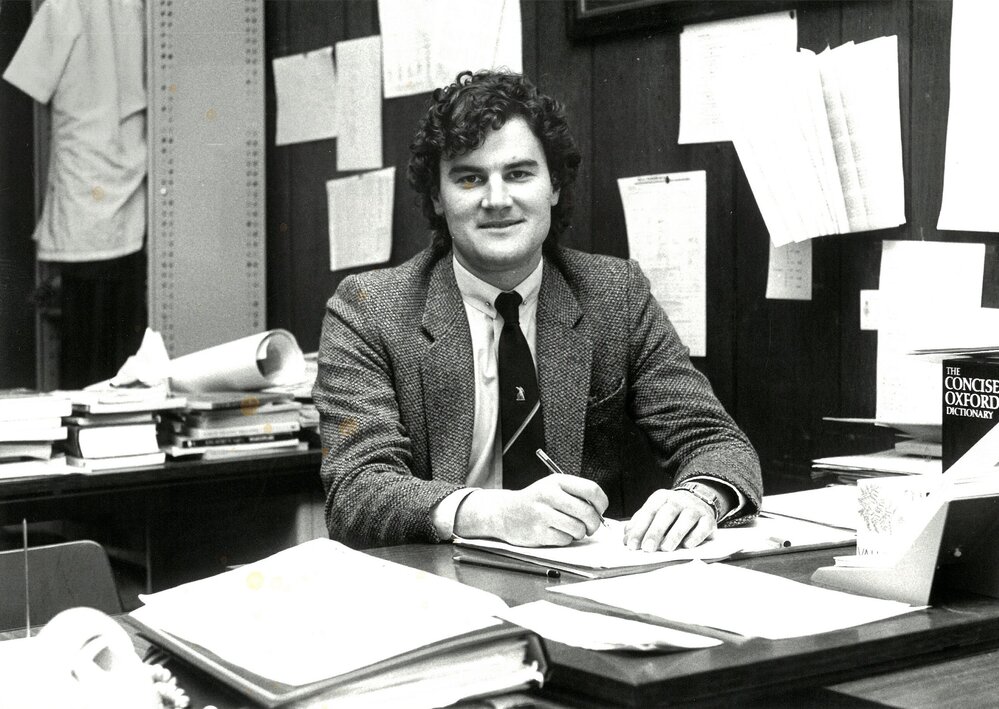 Adrian Collins seated at desk, circa 1990