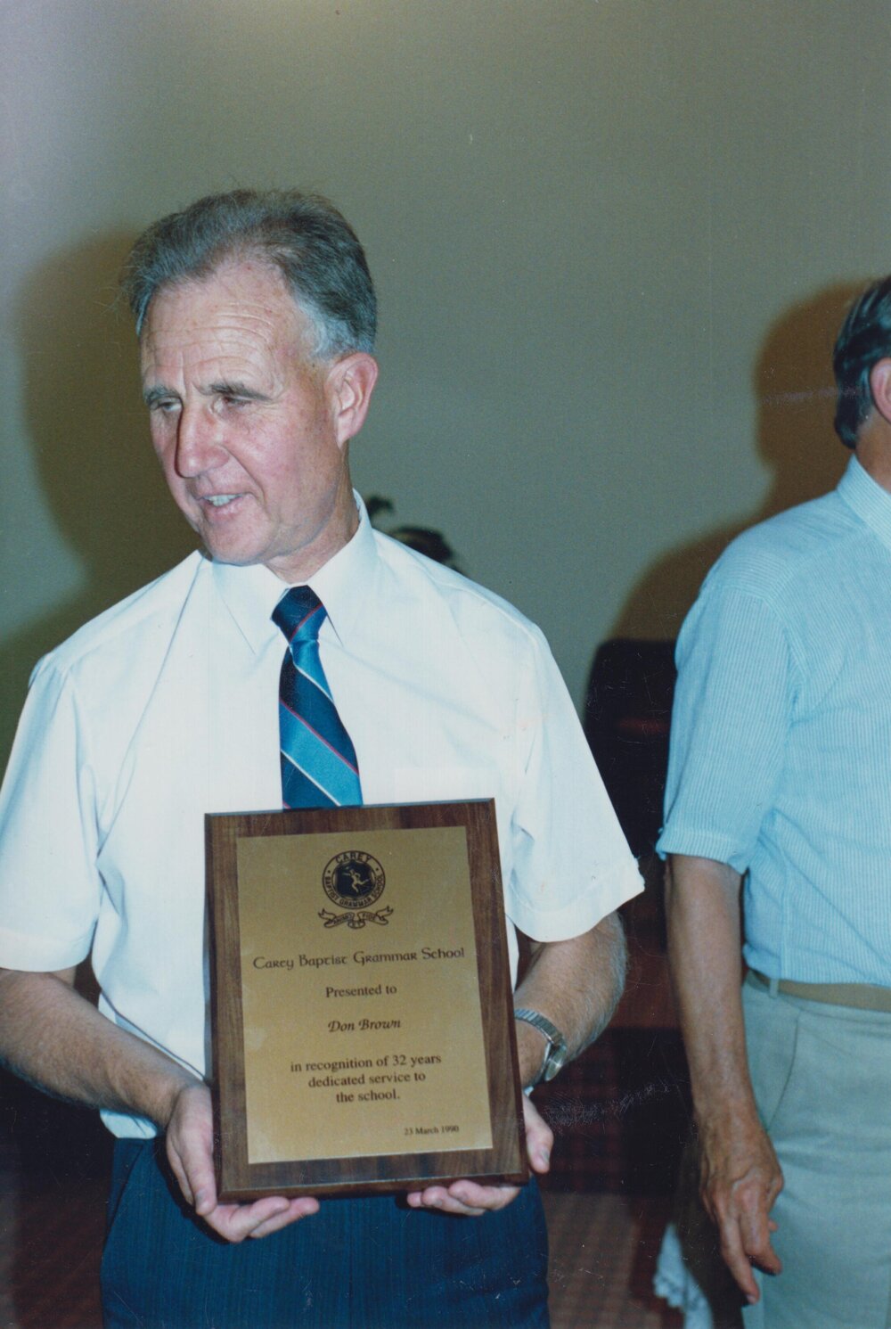 Mr Don Brown holding award recognising his 32 years dedicated service to the school, 1990