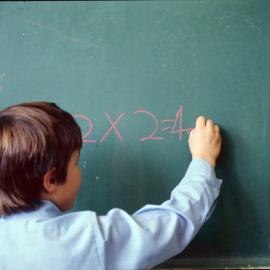 Junior School boy writing mathematical equation on chalkboard, 1974