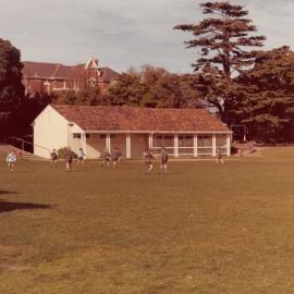 Playing on the Junior School oval with pavilion in background, 1975