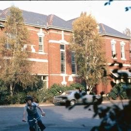 Student riding bicycle in front of Urangeline, 1974